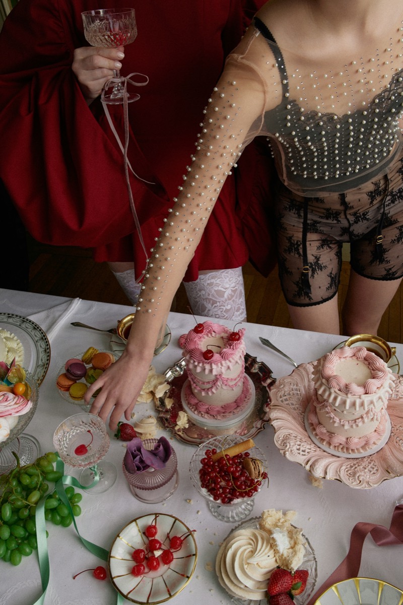 a dessert table of pink cakes, cherries, and a pearled glove